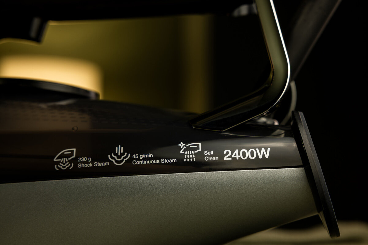 Zbliżenie czarnego żelazka z tekstem pokazującym uderzenie pary, ciągłą parę, samooczyszczanie i moc w watach.