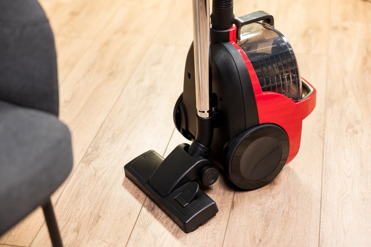 Czerwono-czarny odkurzacz z czarną szczotką na drewnianej podłodze, obok krzesła.