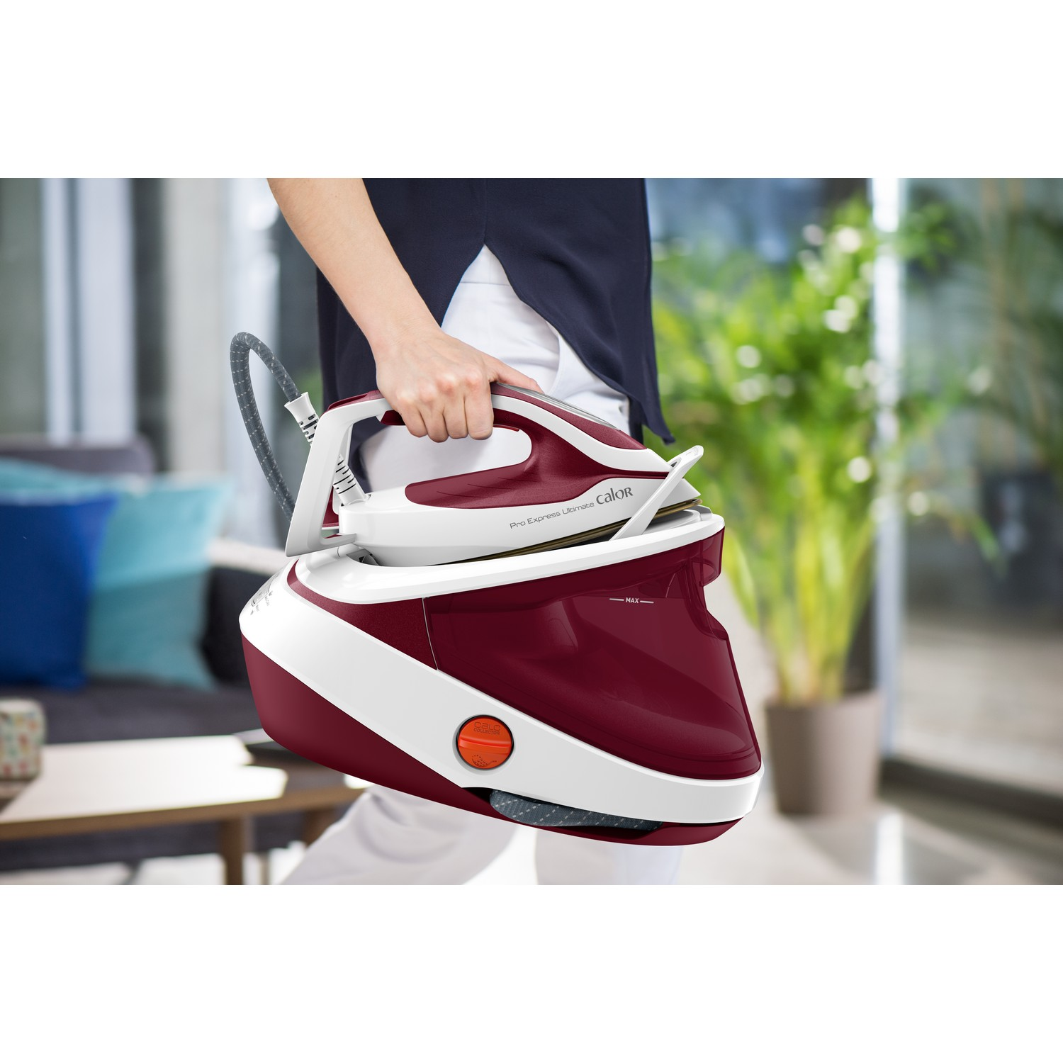 A person holding a red and white iron, steam generator is in the background.