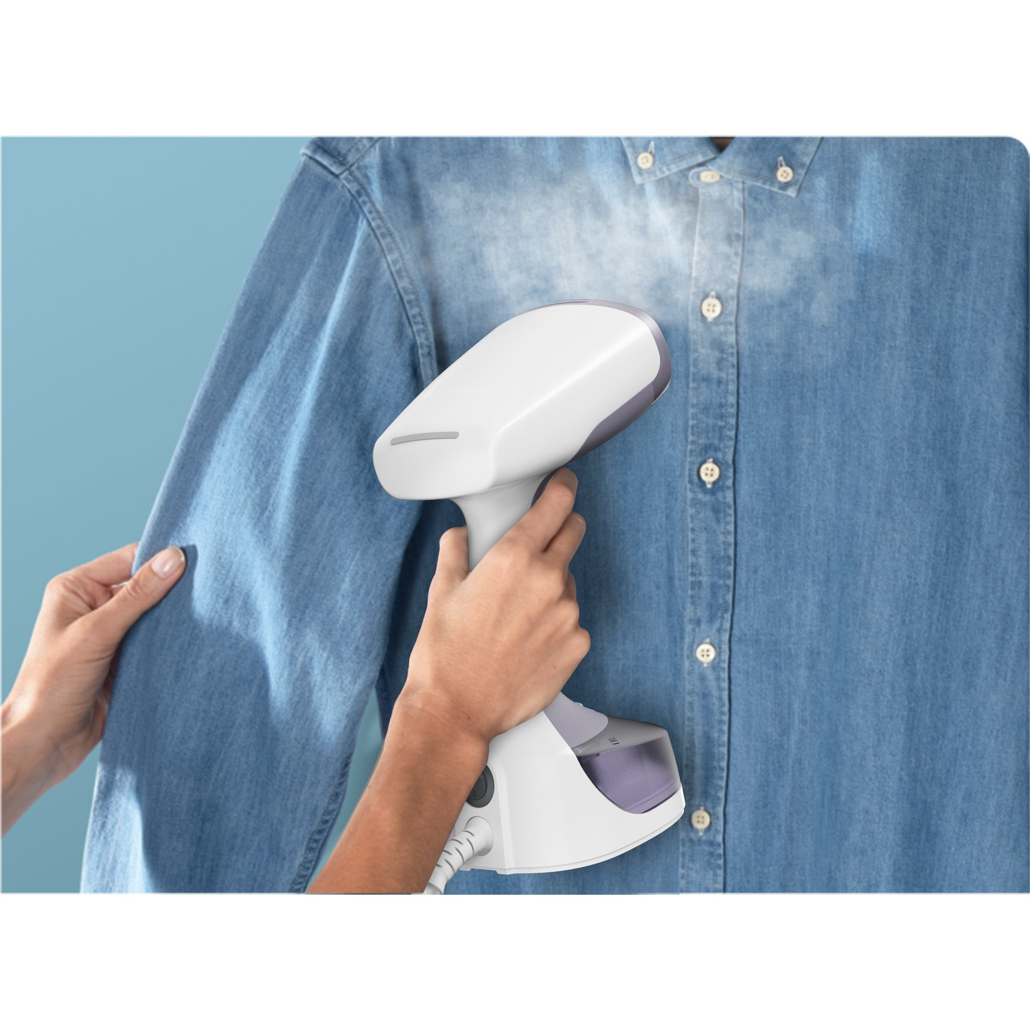 Mains d'une personne utilisant un défroisseur blanc pour défroisser une chemise en jean bleue, en gros plan.