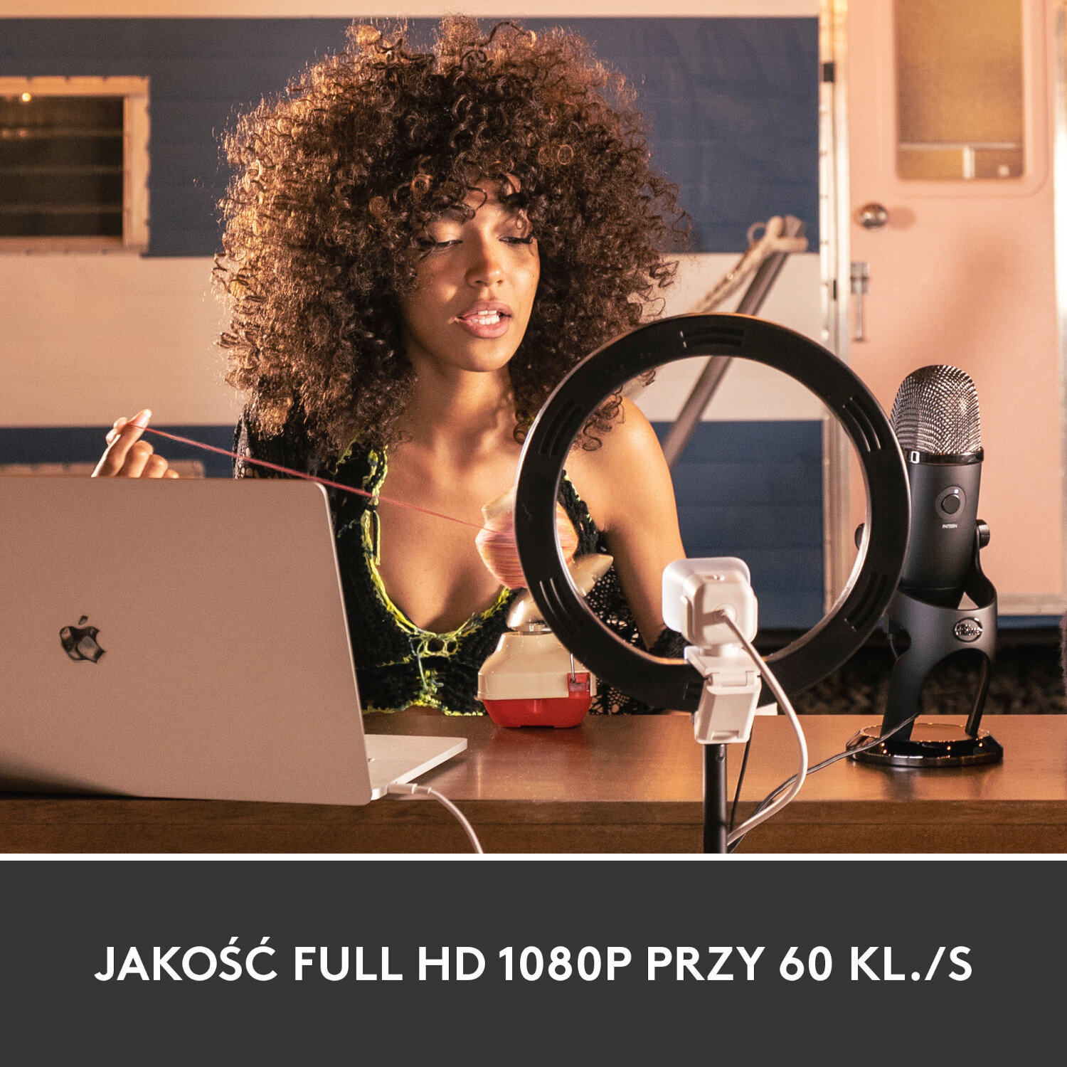 Kobieta z kręconymi włosami nagrywa. Używa laptopa, lampy pierścieniowej i mikrofonu. Tło to pokój.