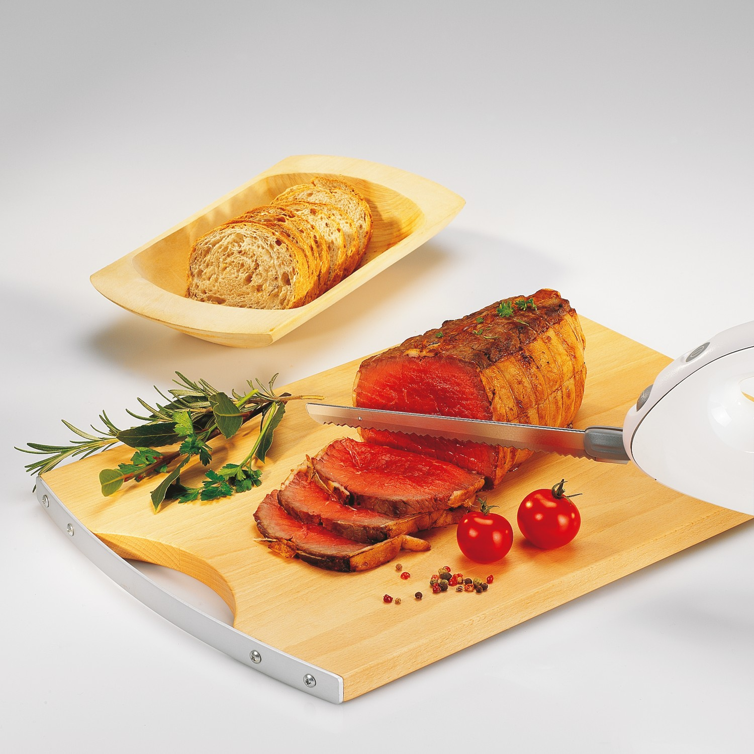 Slices of roast beef on a wooden board with tomatoes and herbs.