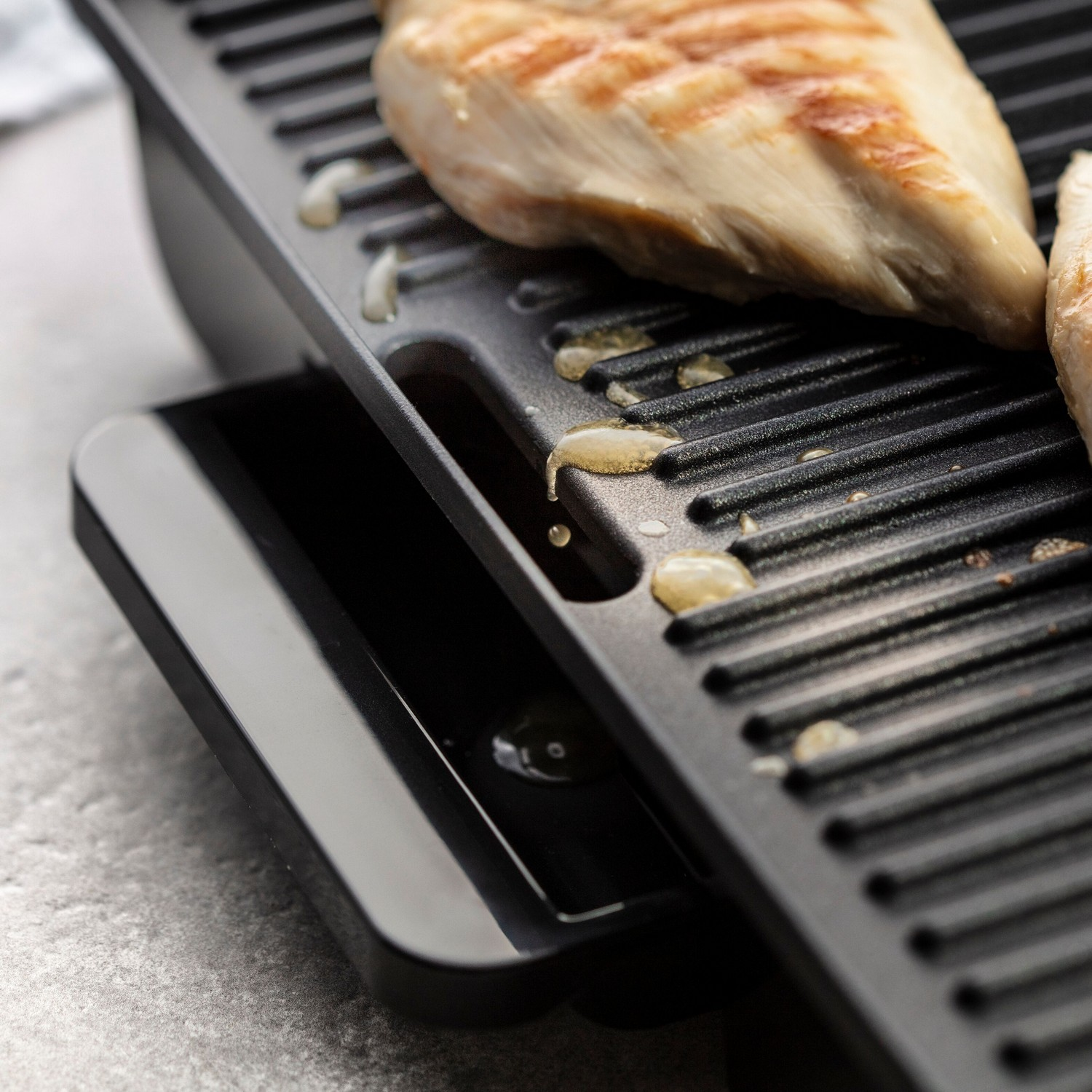 Poitrine de poulet grillée sur une plaque noire avec des gouttes d'huile, gros plan sur une surface blanche.