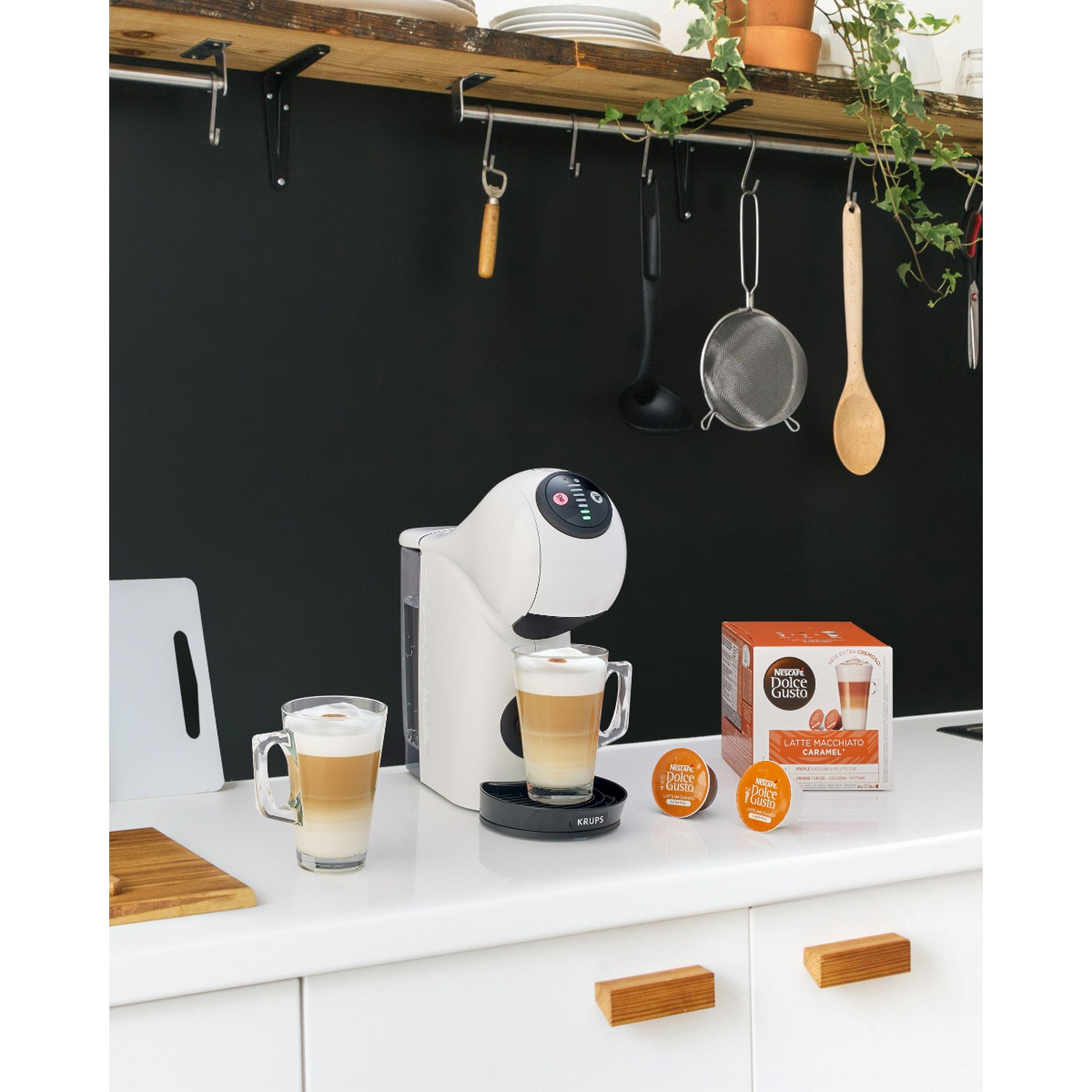 Keuken met koffiezetapparaat, bekers en koffiepads op een wit aanrecht.