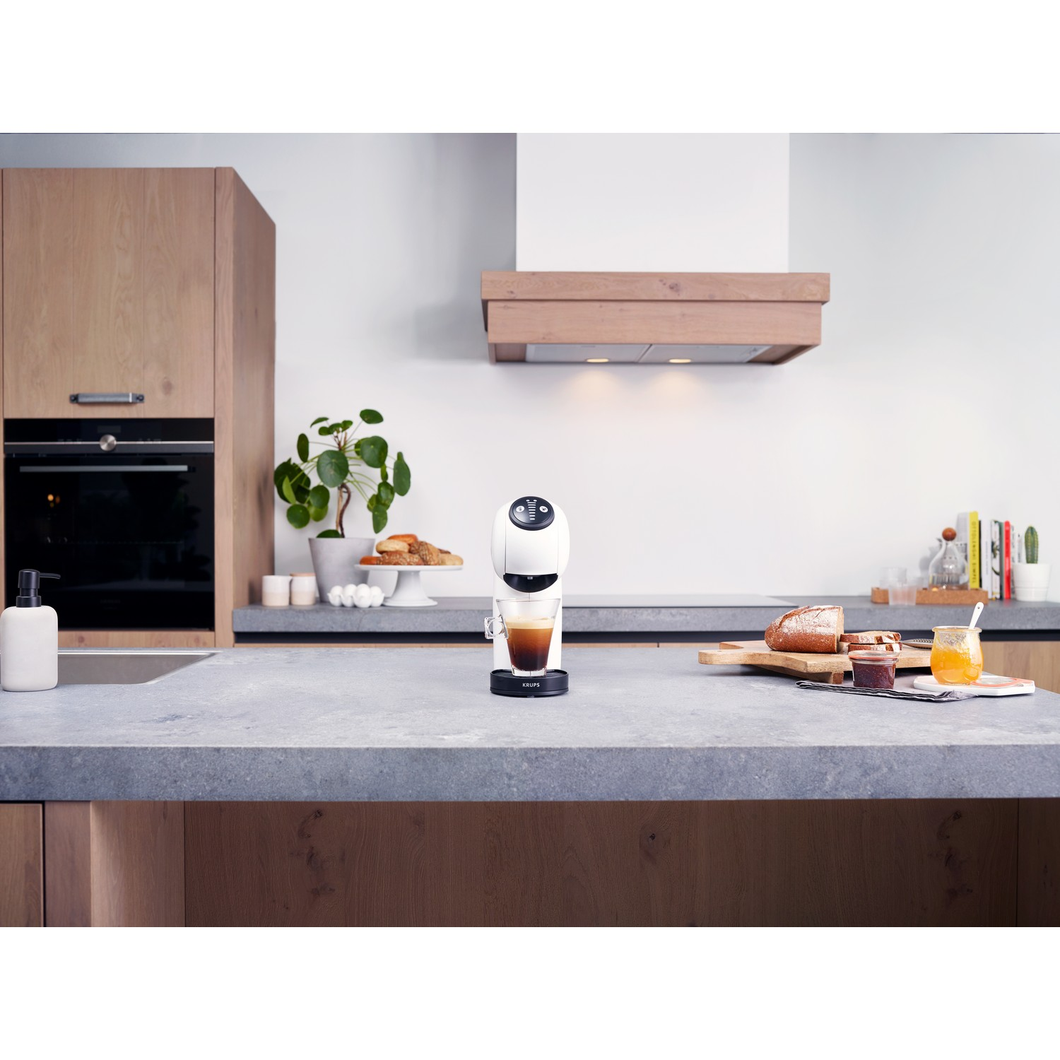 Een witte koffiemachine met een glas koffie op een aanrecht, keukenachtergrond met eten.
