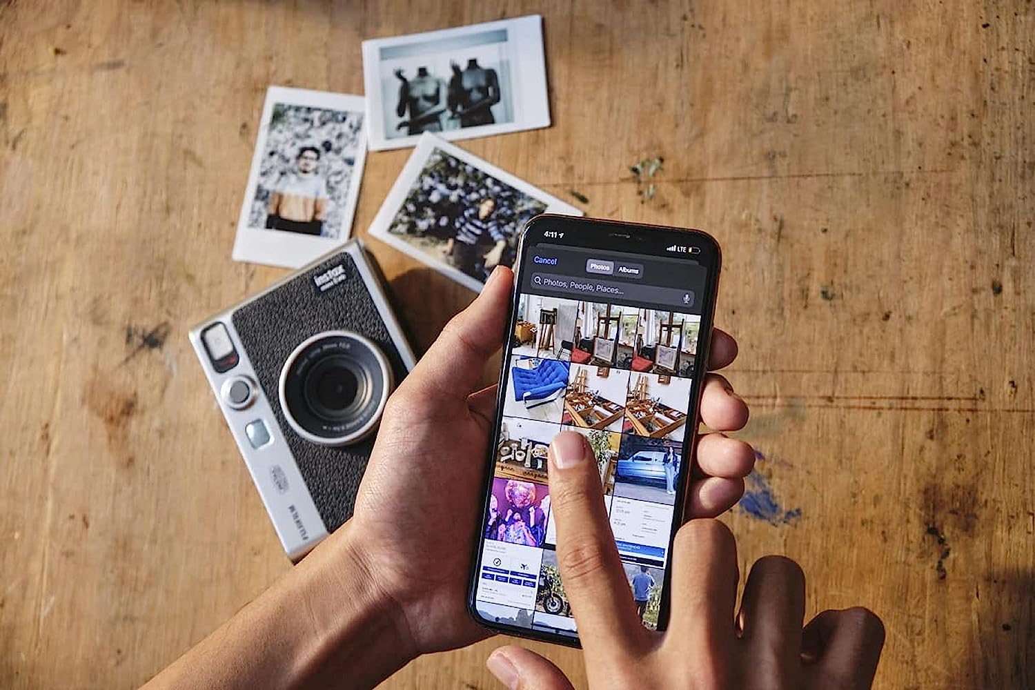 Hand hält Telefon mit Fotos. Kamera und Abzüge auf Holztisch.