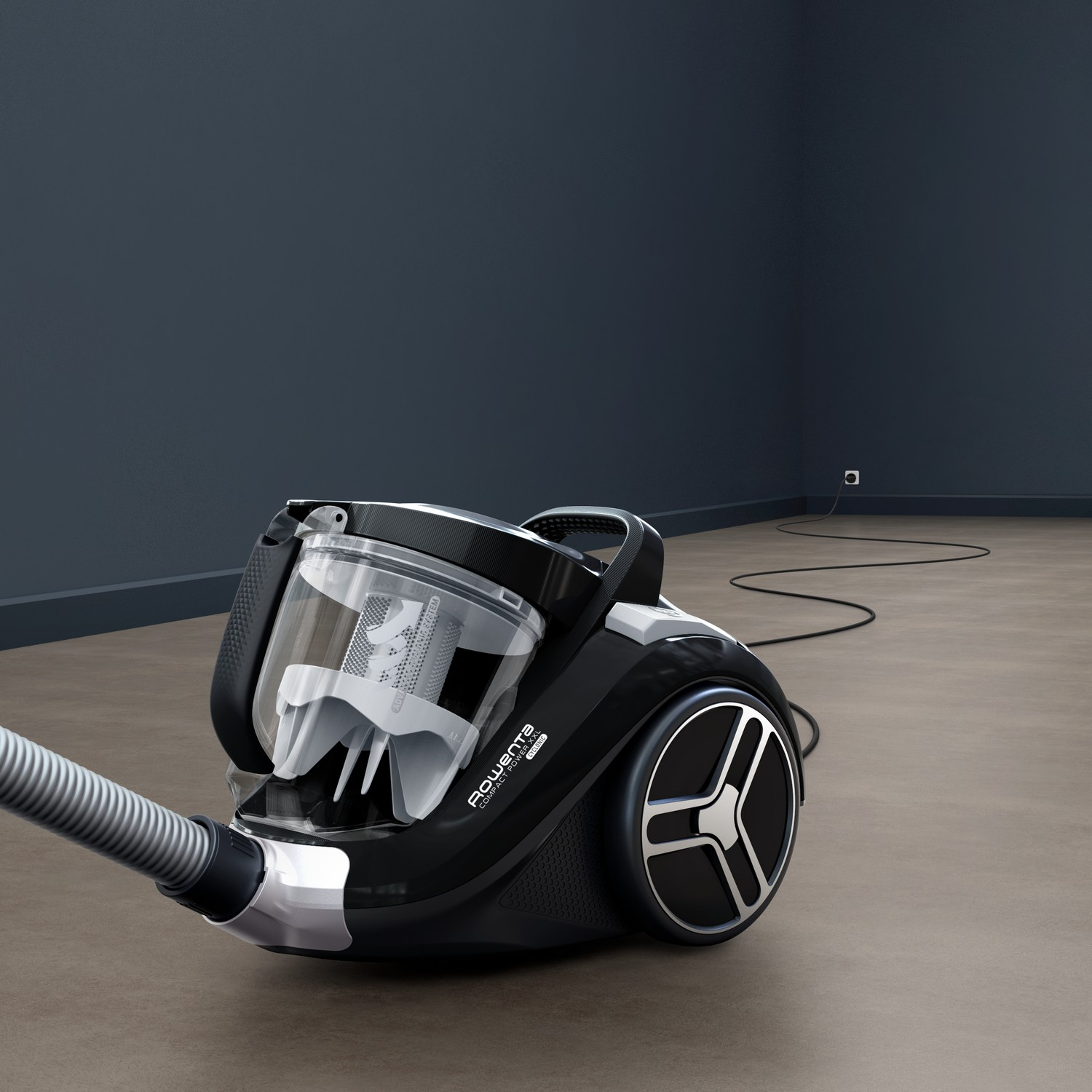 Black vacuum cleaner on a brown floor, angled towards a dark blue wall.