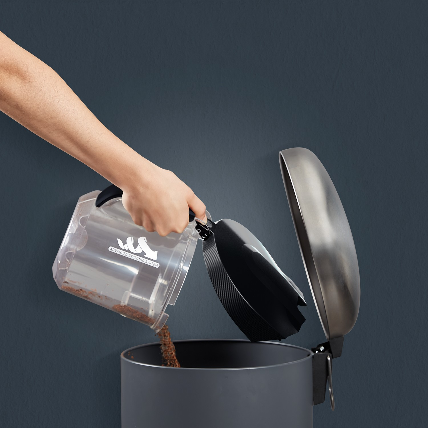 A hand emptying a vacuum cleaner dust container into a trash can. The dust is brown.