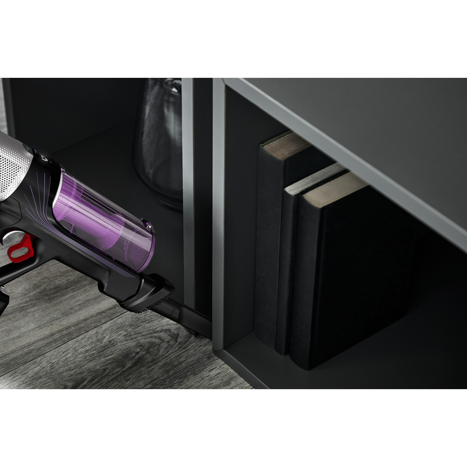 A vacuum cleaner and a glass vase on top of a cabinet, with books in the background.