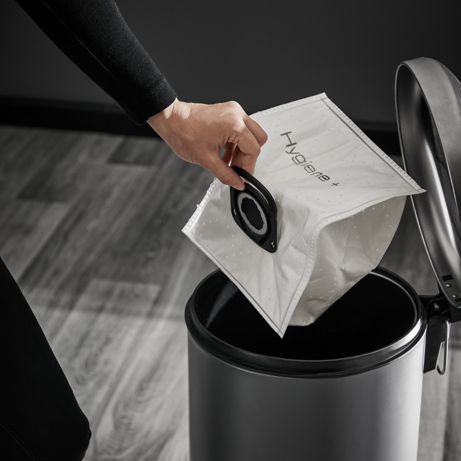 A hand opening a trash can lid, holding a white trash bag.