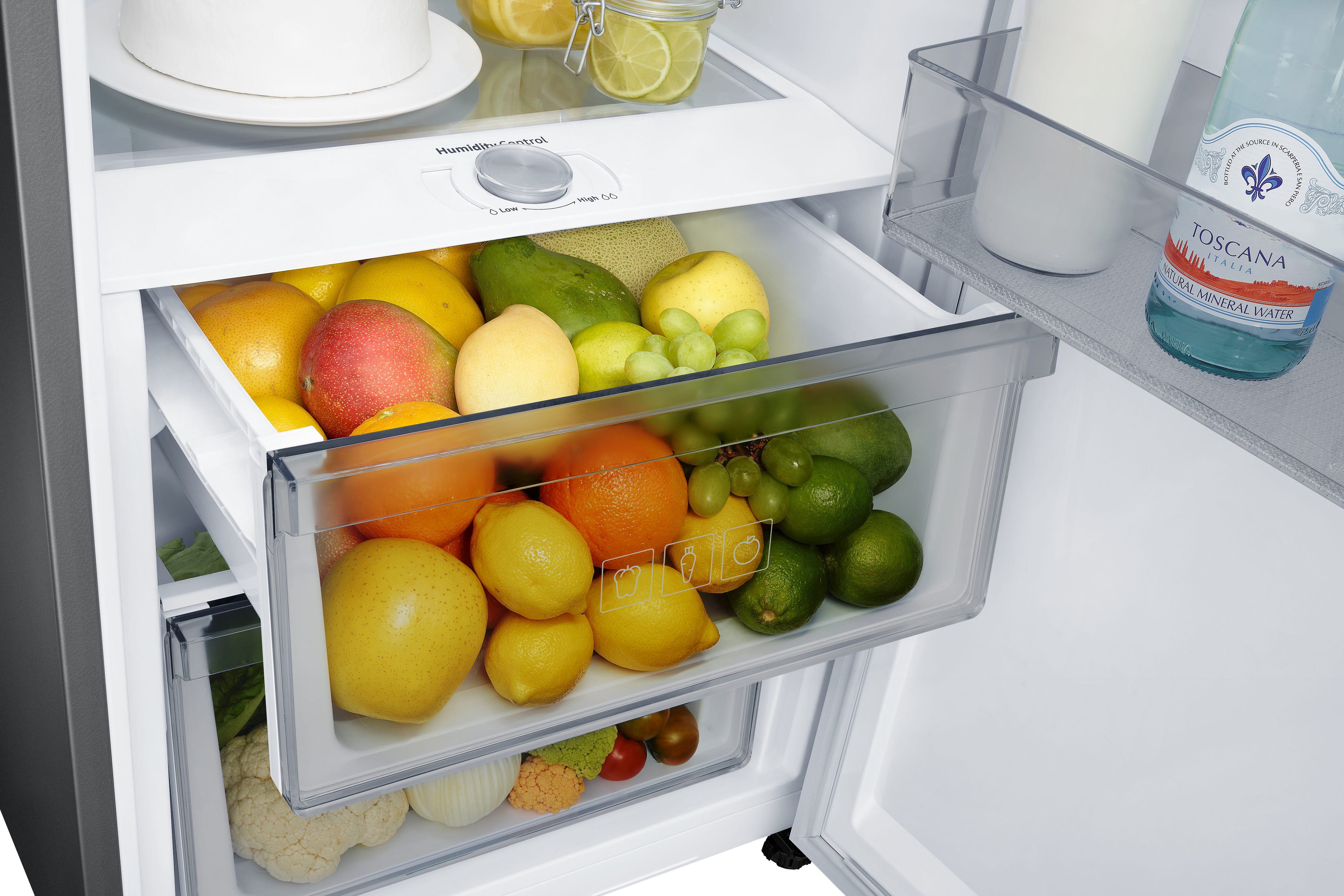 Cajón de refrigerador lleno de varias frutas. Se ven naranjas, limones y limas.