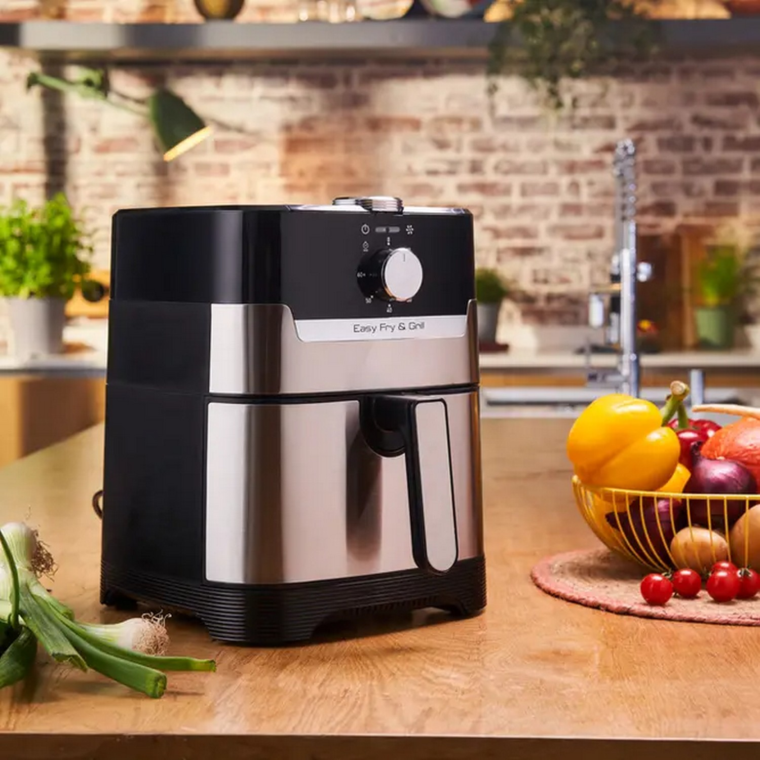 Black and silver air fryer with vegetables. The air fryer is on a wooden table.