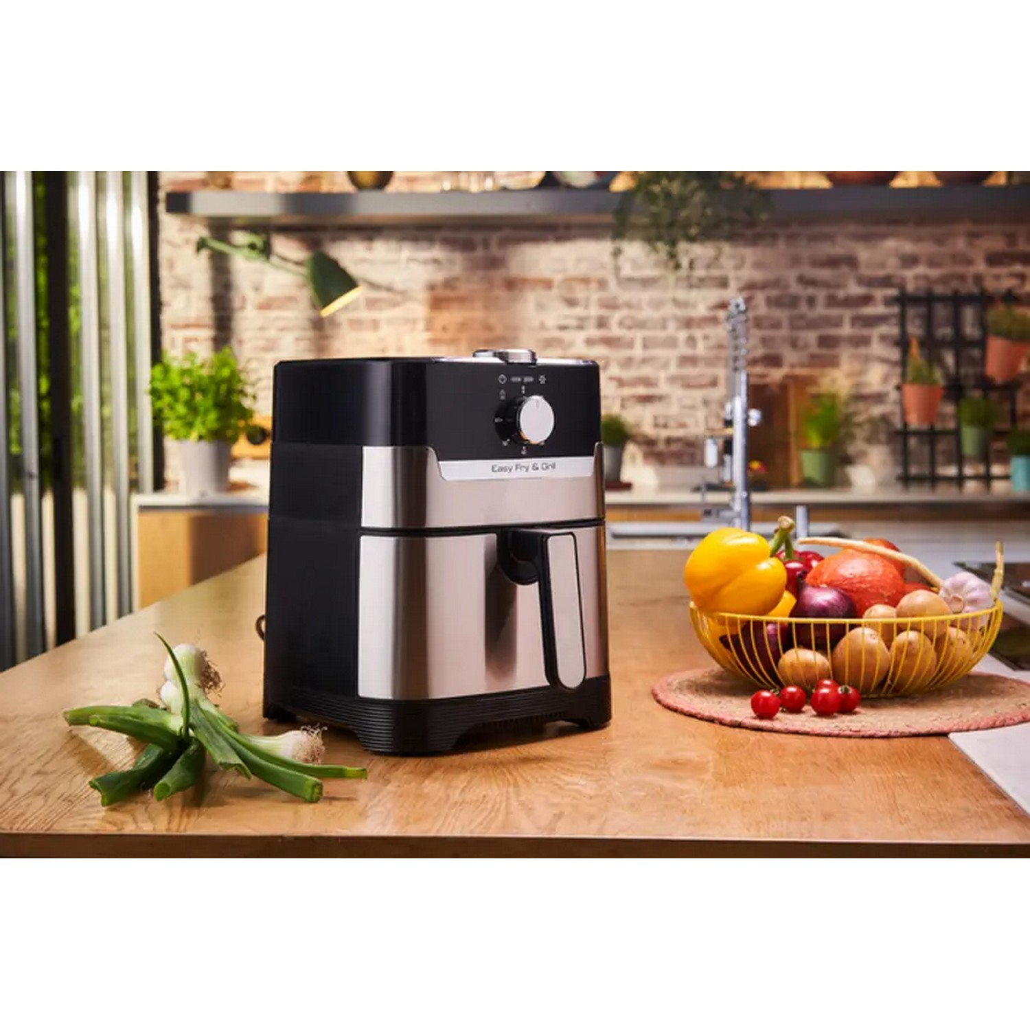 Black and silver air fryer on a wooden surface with vegetables and kitchen utensils.