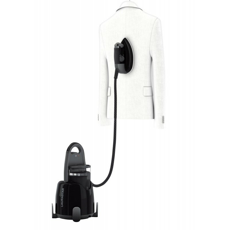 Czarny parownik do ubrań parujący białą kurtkę. Parownik stoi na podłodze.