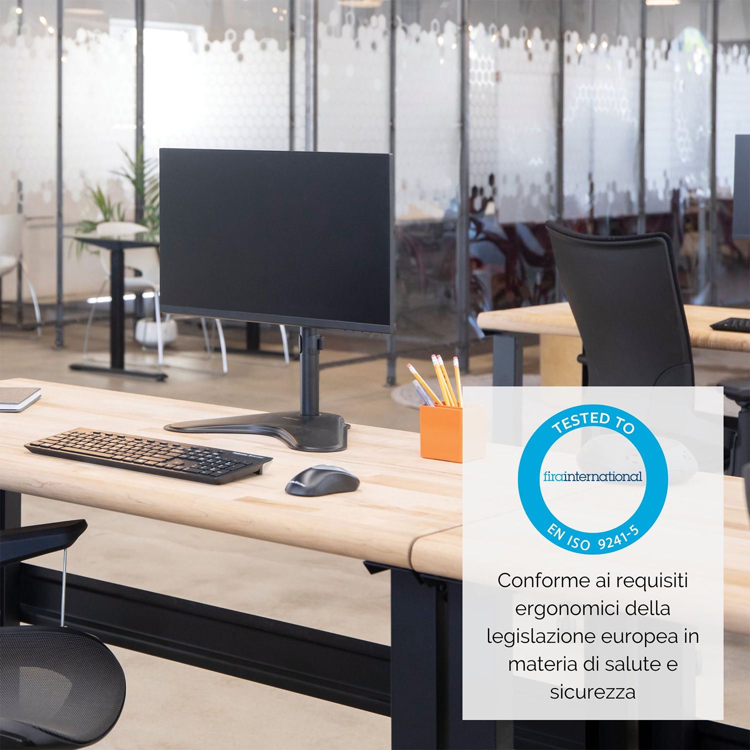 Una scrivania con una configurazione del computer, tra cui un monitor e una tastiera. Un cartello dice Testato secondo EN ISO 9241-5.