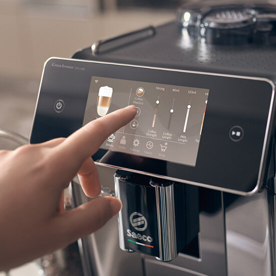 Dłoń na ekranie ekspresu do kawy, wybierająca opcje kawy.