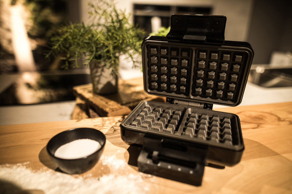 Gofrownica na drewnianym stole. Mała miska cukru i roślina również są widoczne.