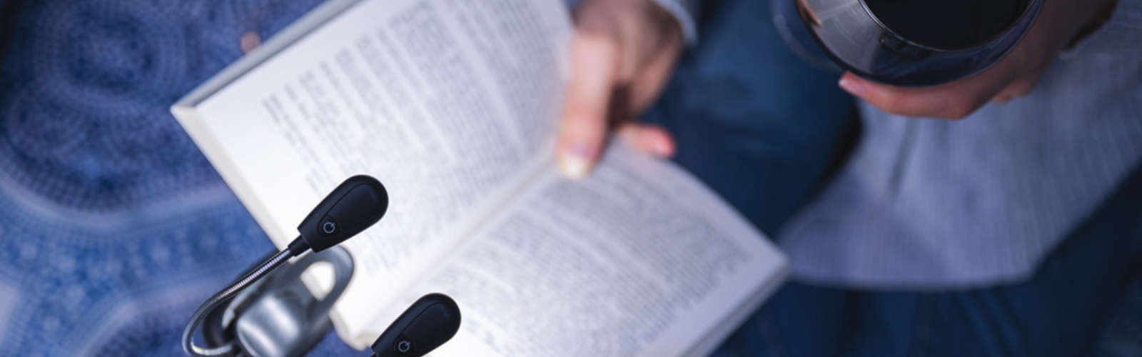 Person liest ein Buch mit Leselampe und hält ein Glas Rotwein.
