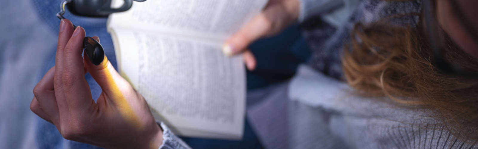 Eine Person liest ein Buch mit einer beleuchteten Fingerlampe. Nur Hände und Buch sichtbar.