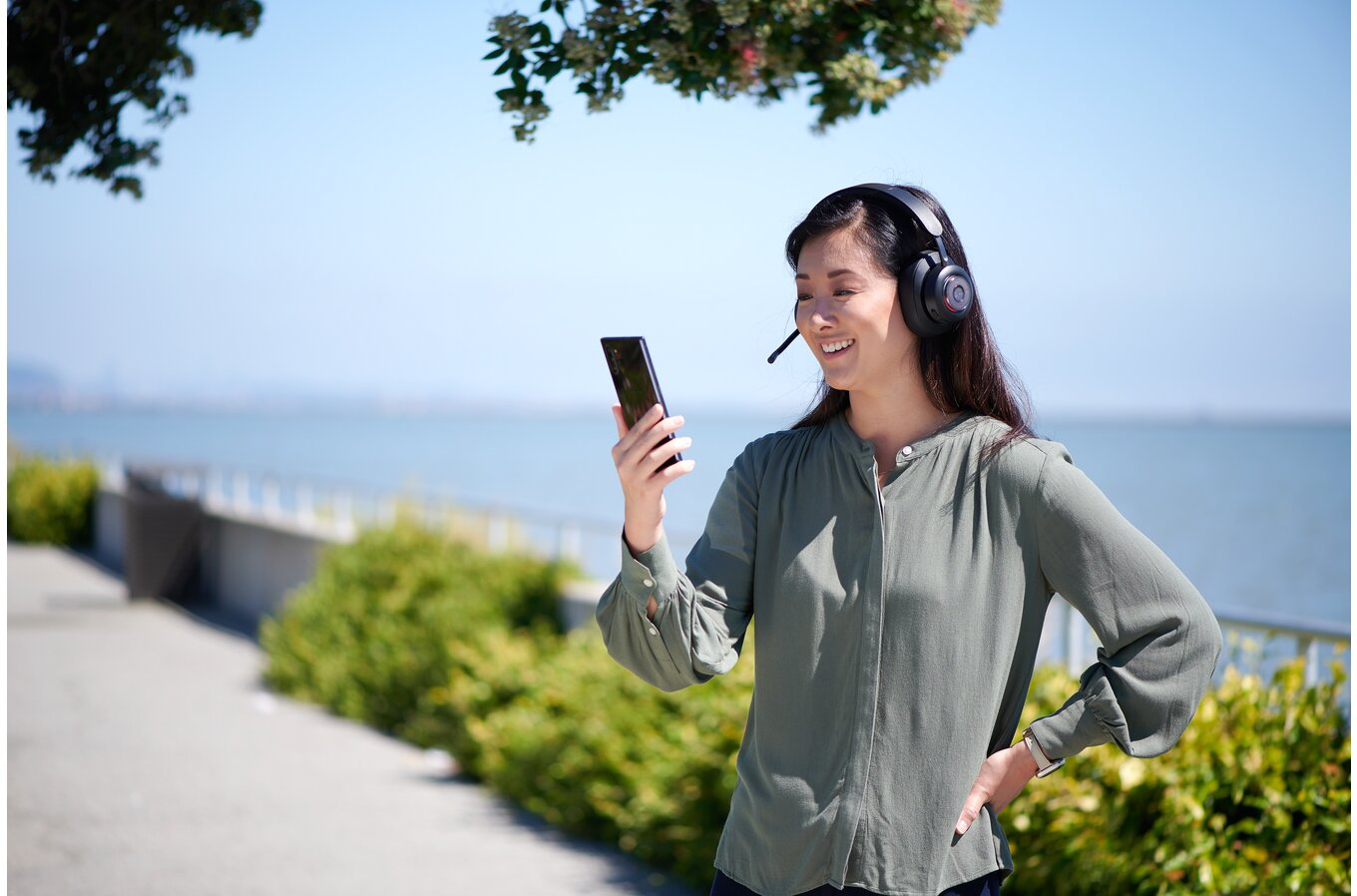 Egy nő headset-tel telefont használ a víz közelében. Mosolyog.