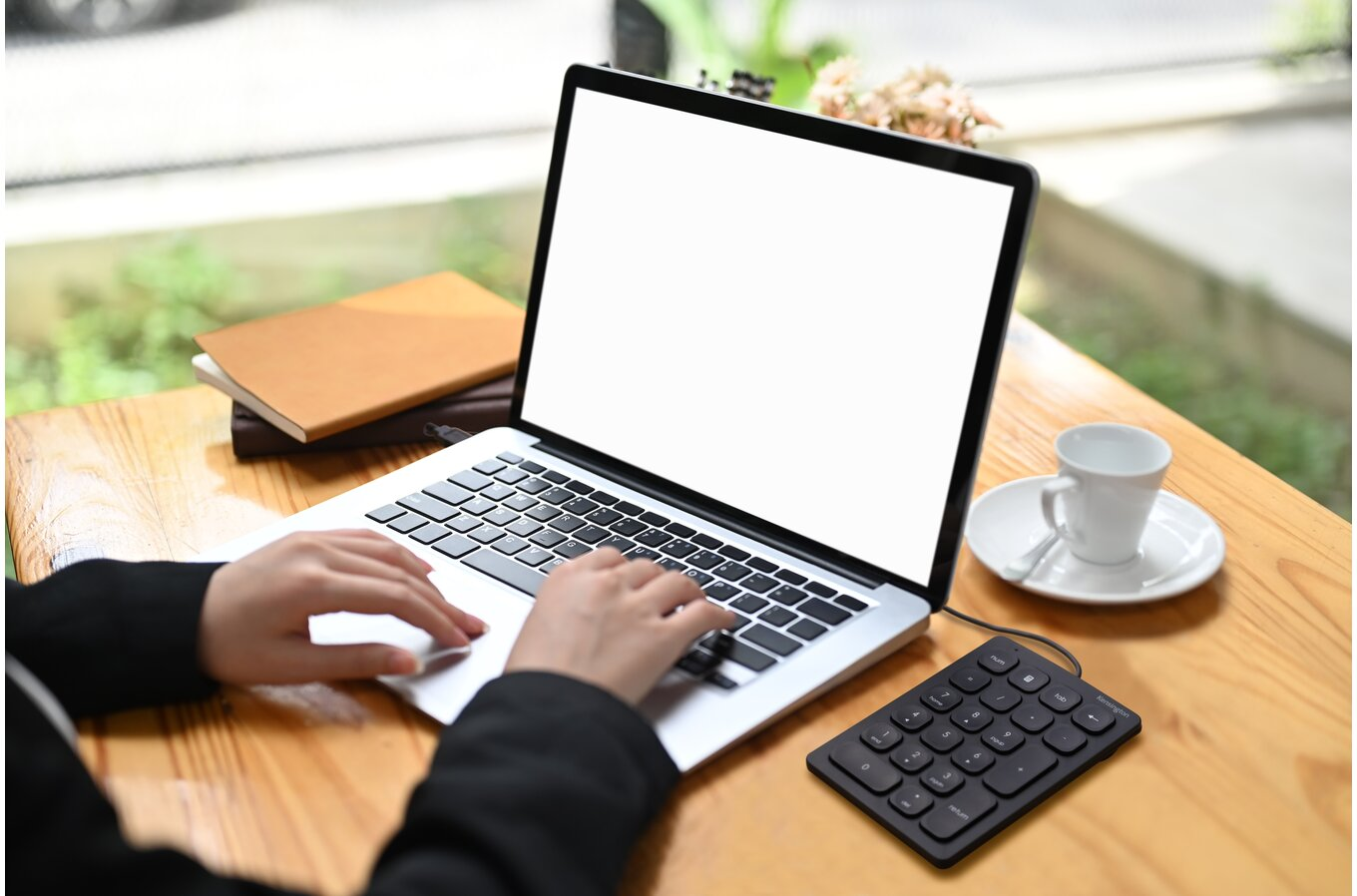 Kéz a laptopon gépel, üres képernyővel, mellette billentyűzet.