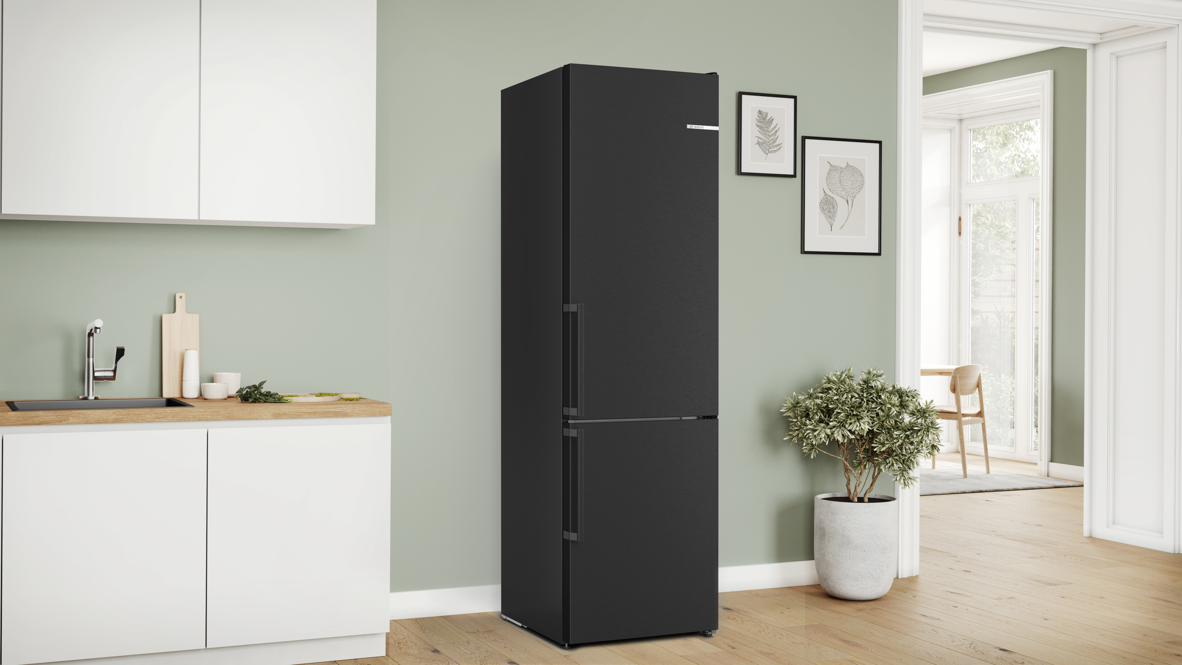 Schwarzer Kühlschrank mit zwei Türen, der vor einer Wand mit Pflanzen und einer Holz-Arbeitsplatte steht.