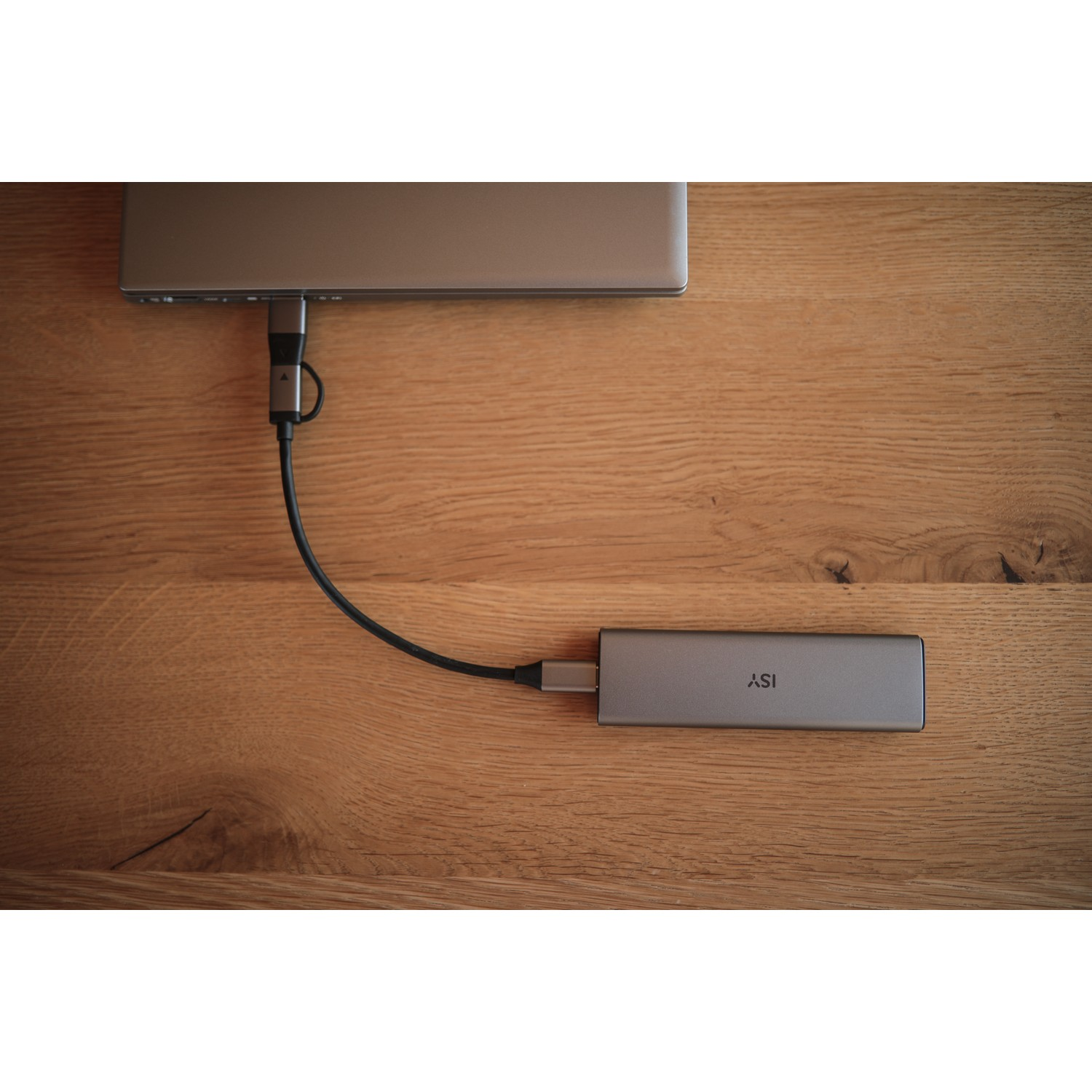 A silver docking station connected to a laptop on a wooden table.