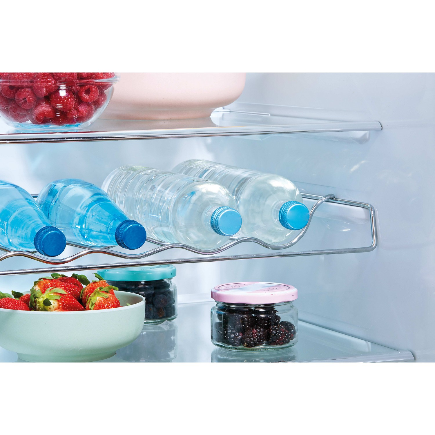 Refrigerator shelf with water bottles and fruit. Berries and a bowl of raspberries are visible.
