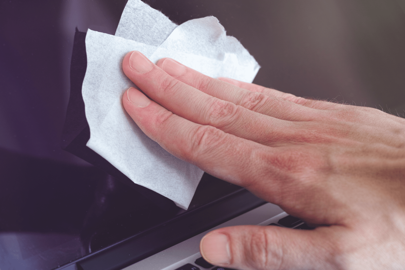 Kéz törli a laptop képernyőjét törlőkendővel.