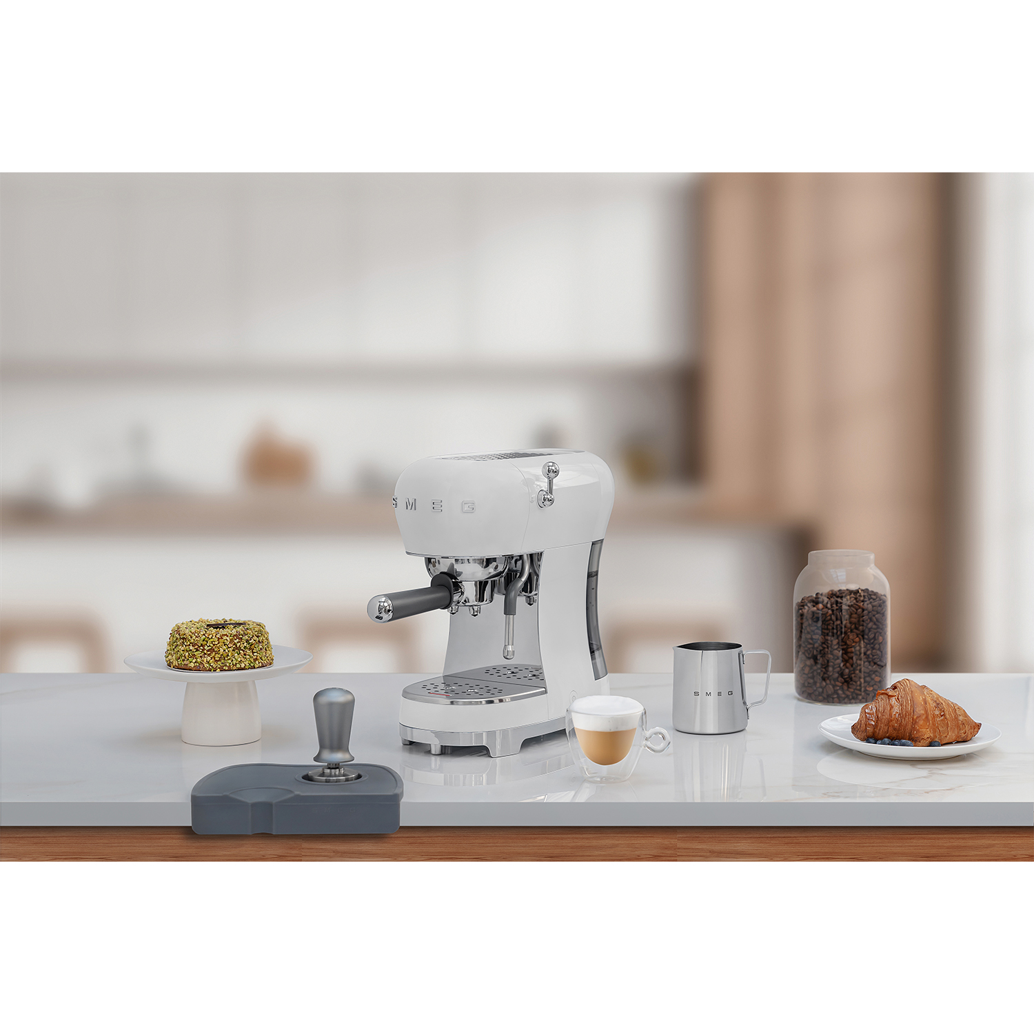 Macchina per espresso Smeg bianca con accessori: tazza, pressino, chicchi, croissant, torta.