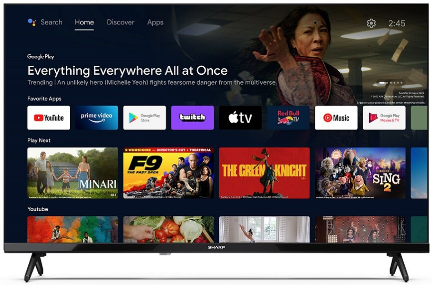 Ekran telewizora wyświetla menu z ikonami aplikacji i plakatem filmowym. Na górze widnieją wyszukiwanie, strona główna, odkrywanie i aplikacje.