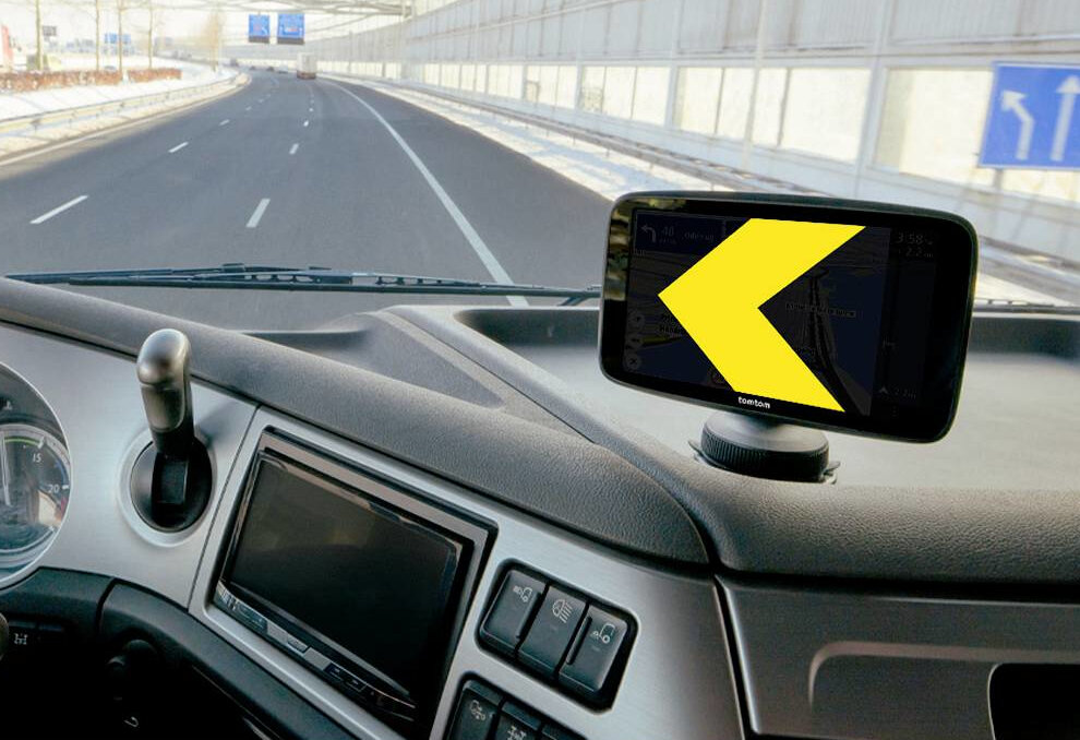 Nawigacja GPS z żółtą strzałką na desce rozdzielczej ciężarówki przed autostradą.