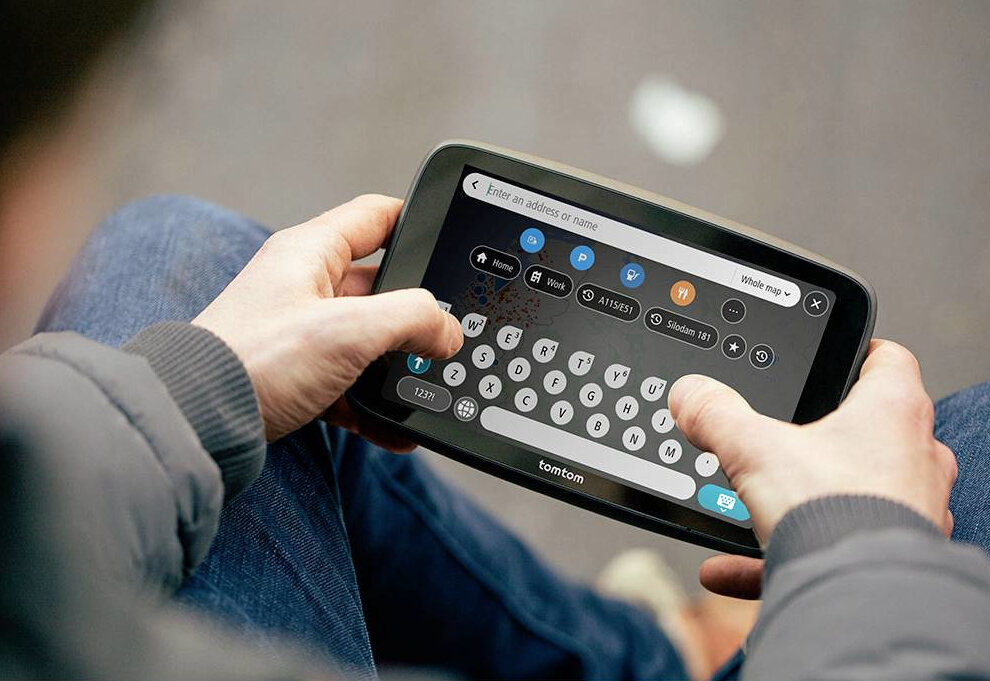 Osoba pisze na urządzeniu nawigacyjnym Tomtom z klawiaturą i mapą.