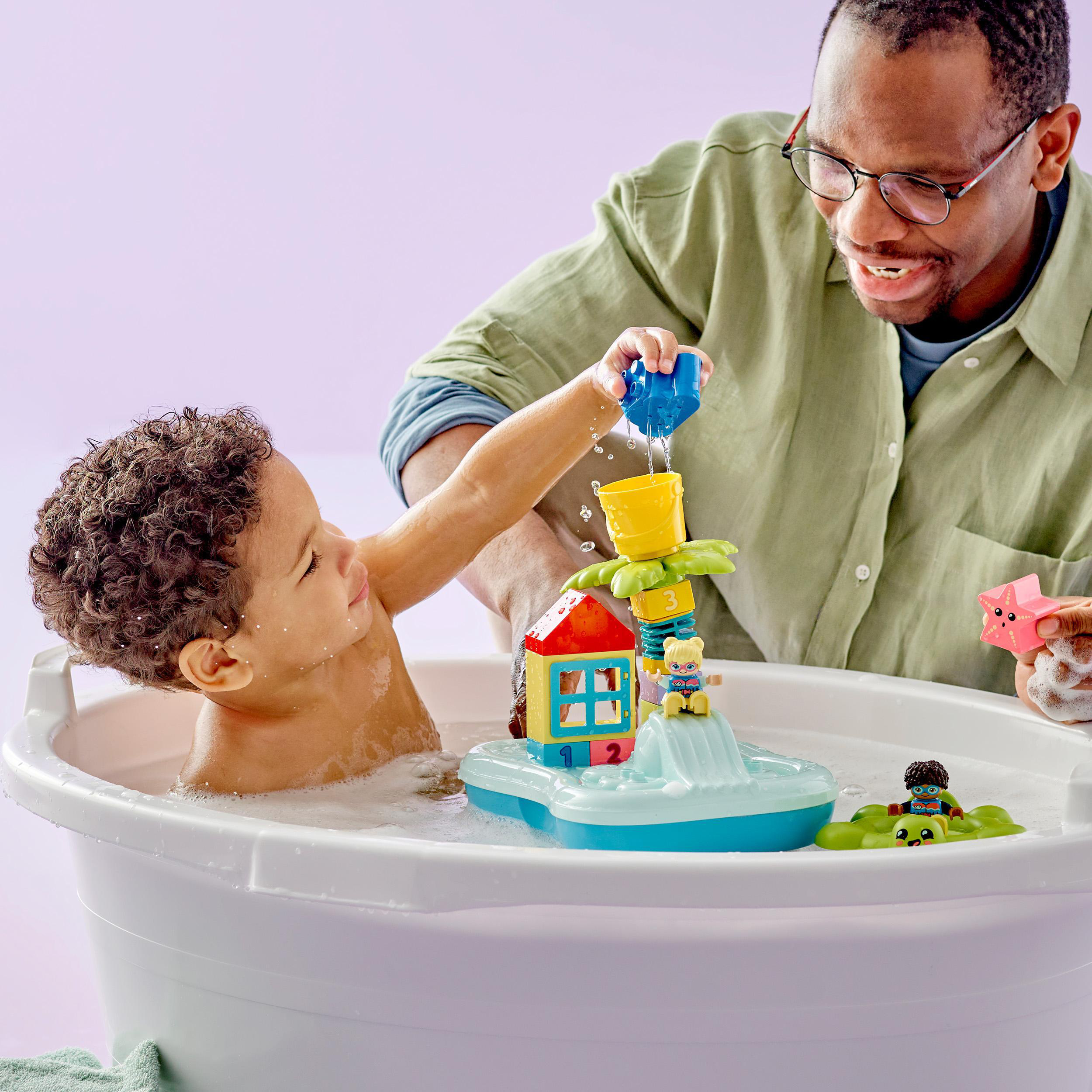 Ein Kind und ein Mann spielen mit Badewannenspielzeug in einer Wanne. Der Mann lächelt, das Kind greift nach Wasser.