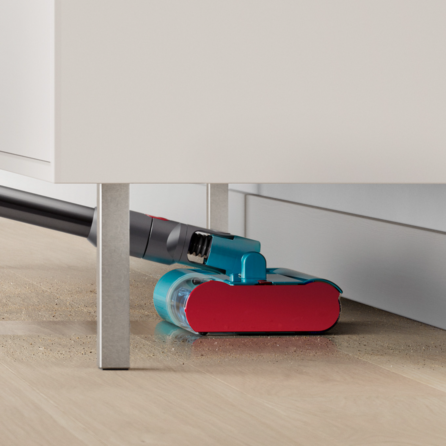 A vacuum cleaner head cleaning under a white cabinet. The head is blue and red, on a wooden floor.
