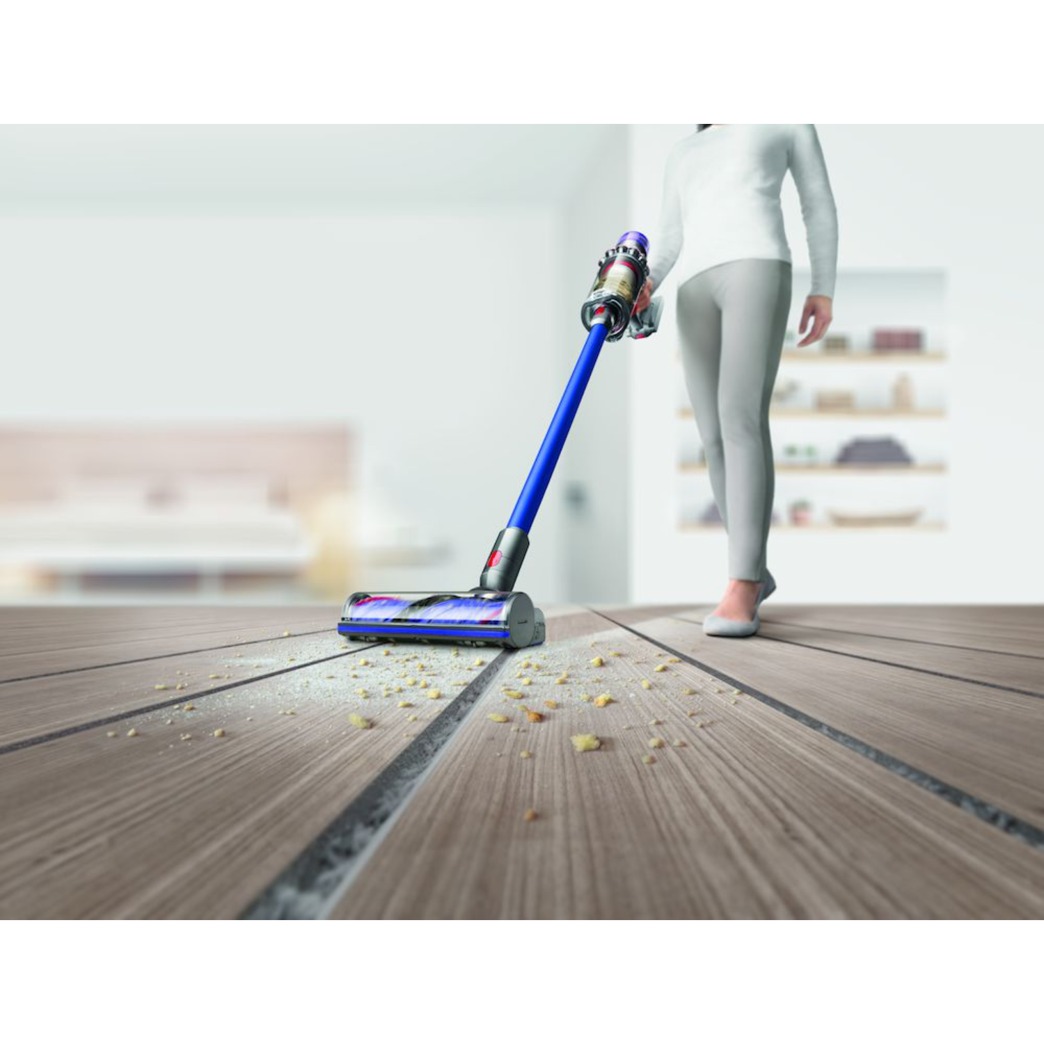 Woman using a blue and silver vacuum cleaner on a wooden floor.