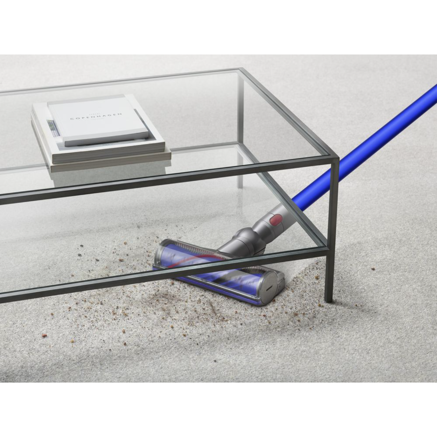 Vacuum cleaner cleaning carpet, coffee table with books on the left.