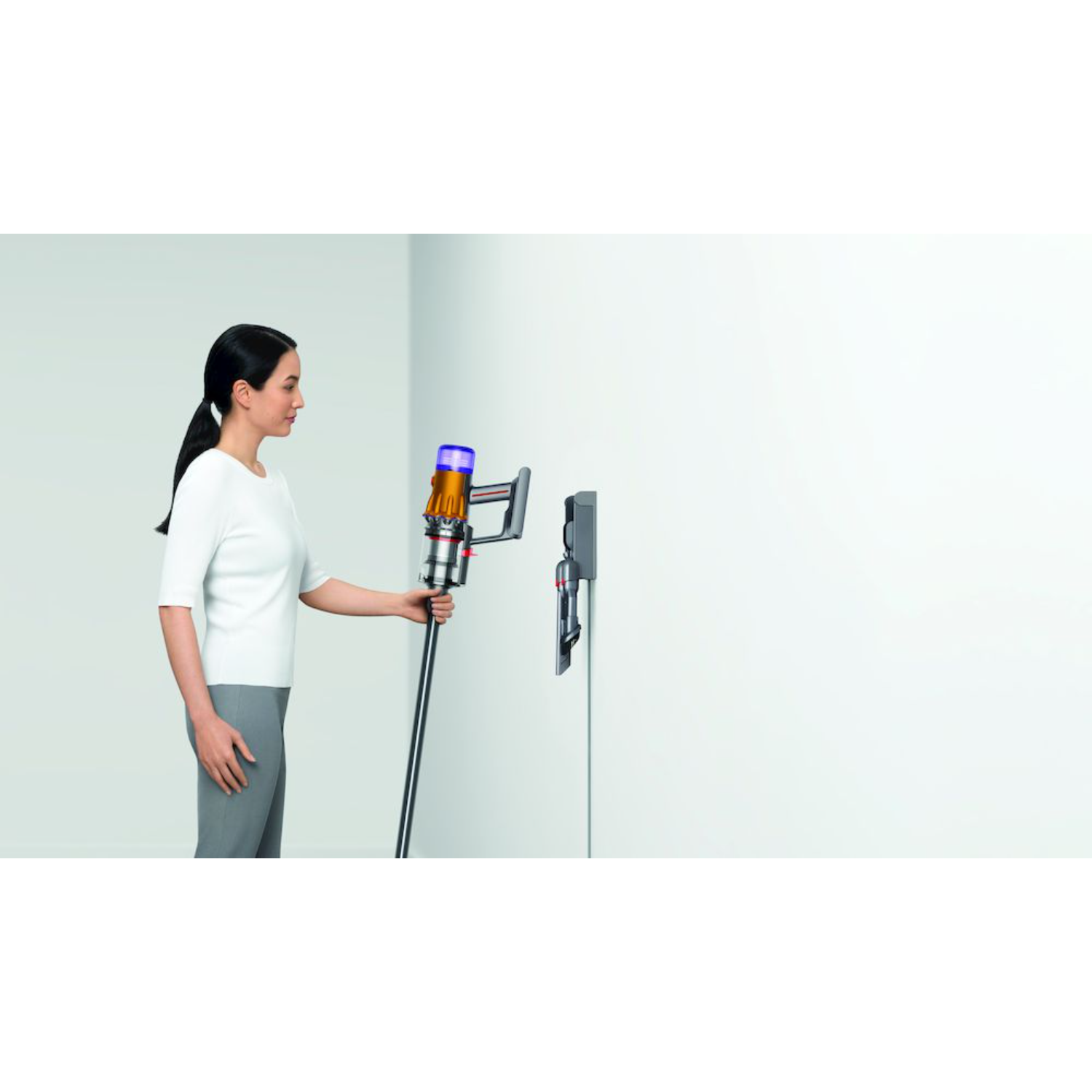Vrouw die een Dyson stofzuiger vasthoudt en in het oplaadstation plaatst.