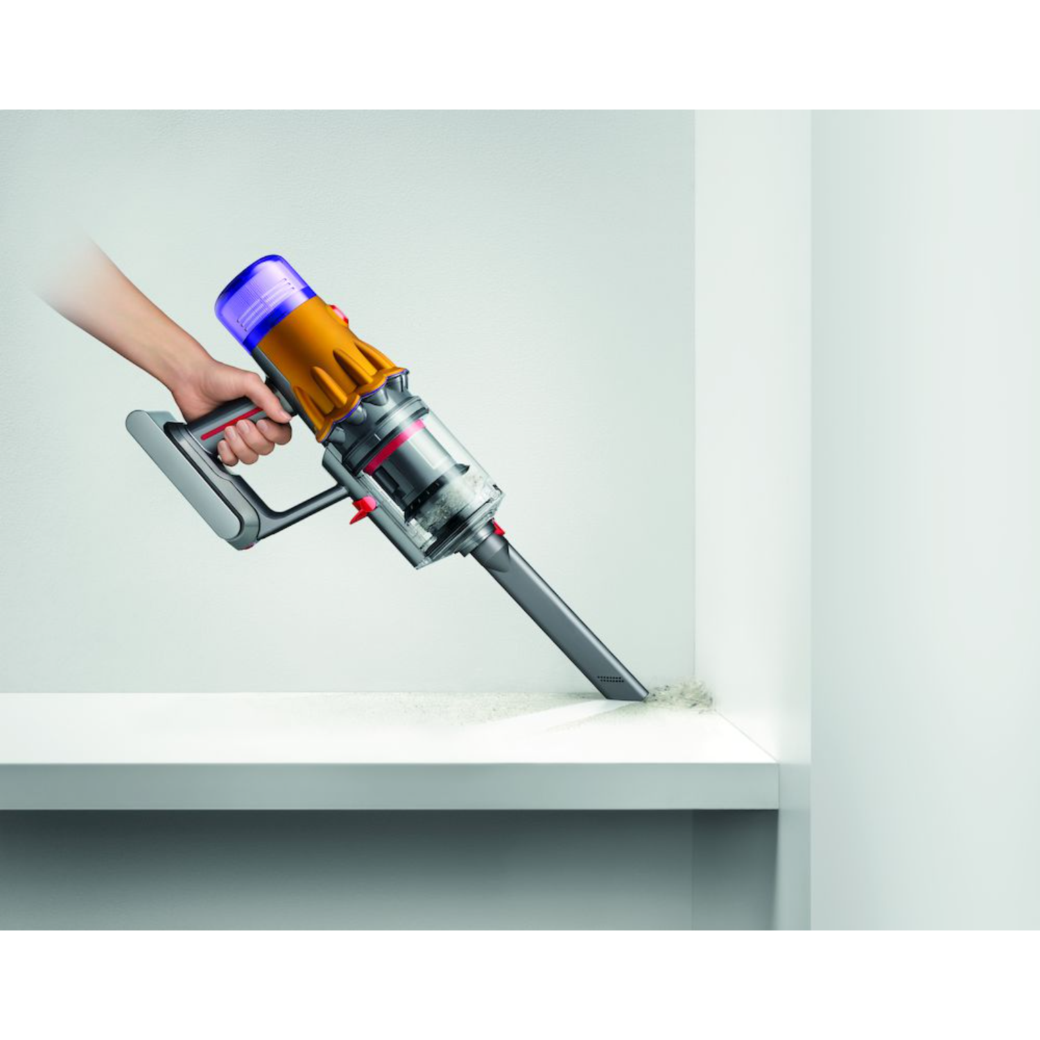 Hand houdt een Dyson stofzuiger vast, maakt een witte plank schoon. Beige stof zichtbaar.