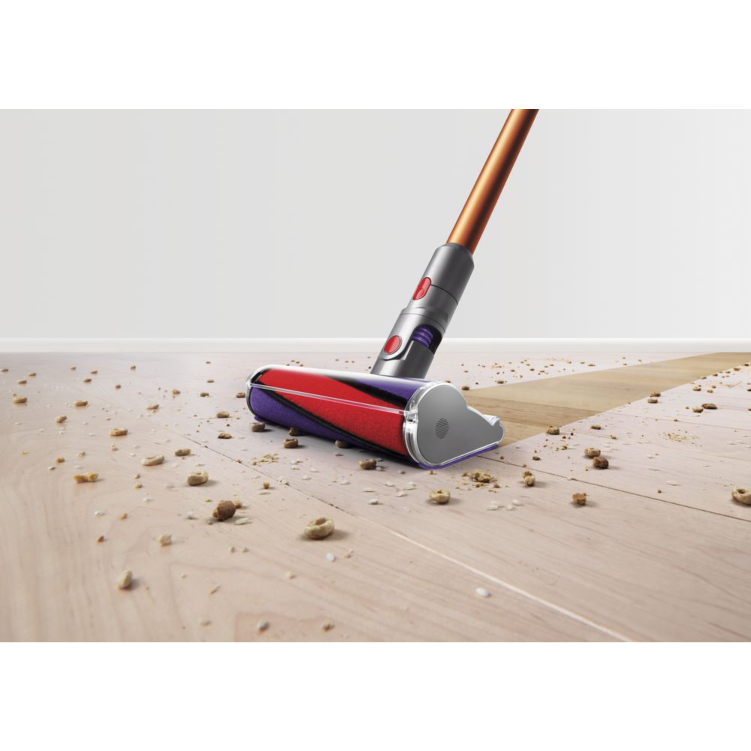 Stofzuiger die een houten vloer schoonmaakt. De stofzuigerkop heeft een paarse en rode rol, en bruin puin.