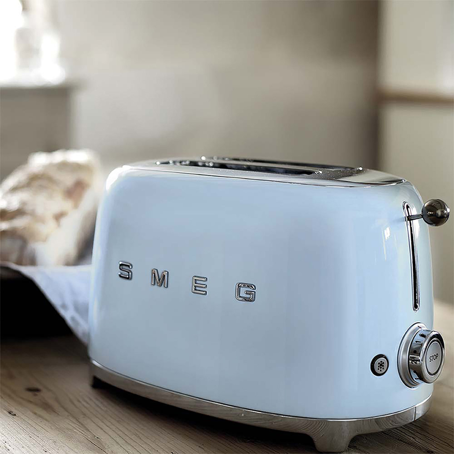 Un tostapane SMEG blu e argento, con una fetta di pane. È su una superficie di legno.
