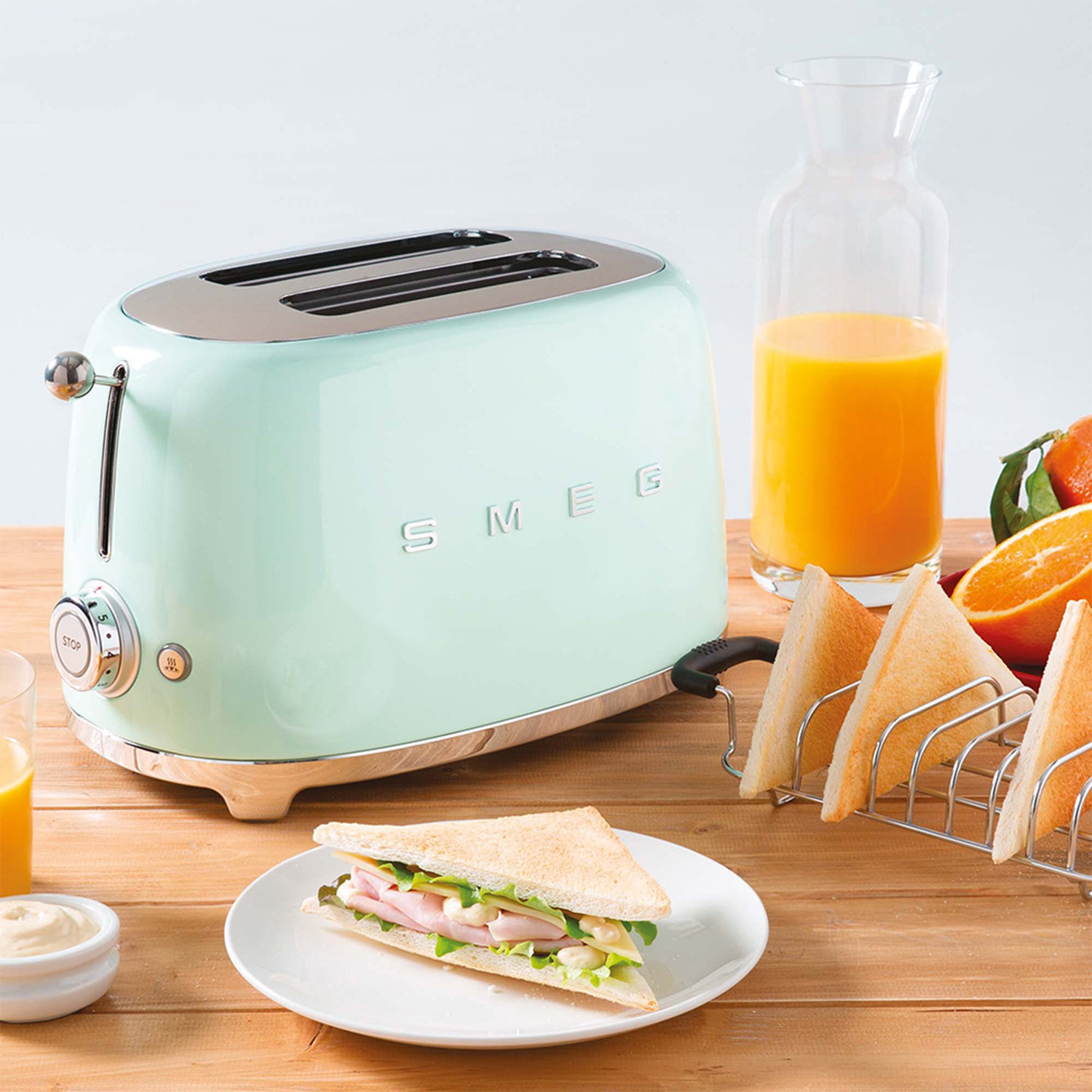 Tostapane SMEG verde menta con un sandwich e una bottiglia di succo su un tavolo di legno.