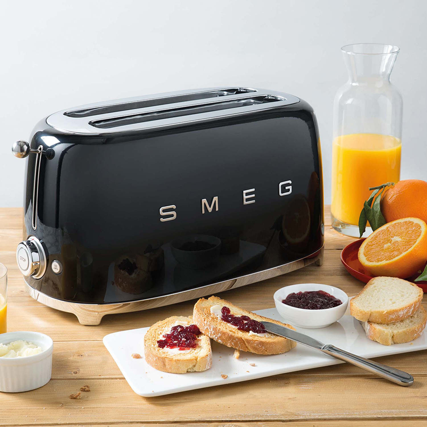 Tostapane SMEG nero con toast, marmellata e succo d'arancia su un tavolo di legno.