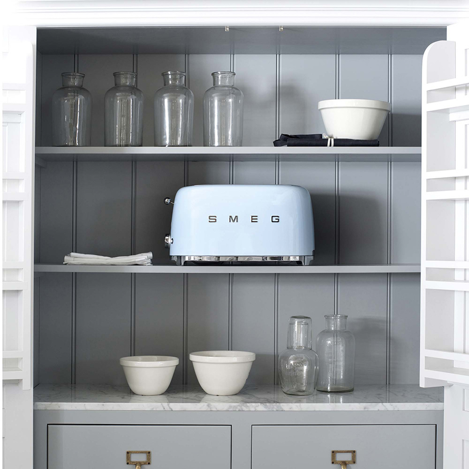 Un tostapane SMEG azzurro in un mobile bianco con ripiani e cassetti grigi.
