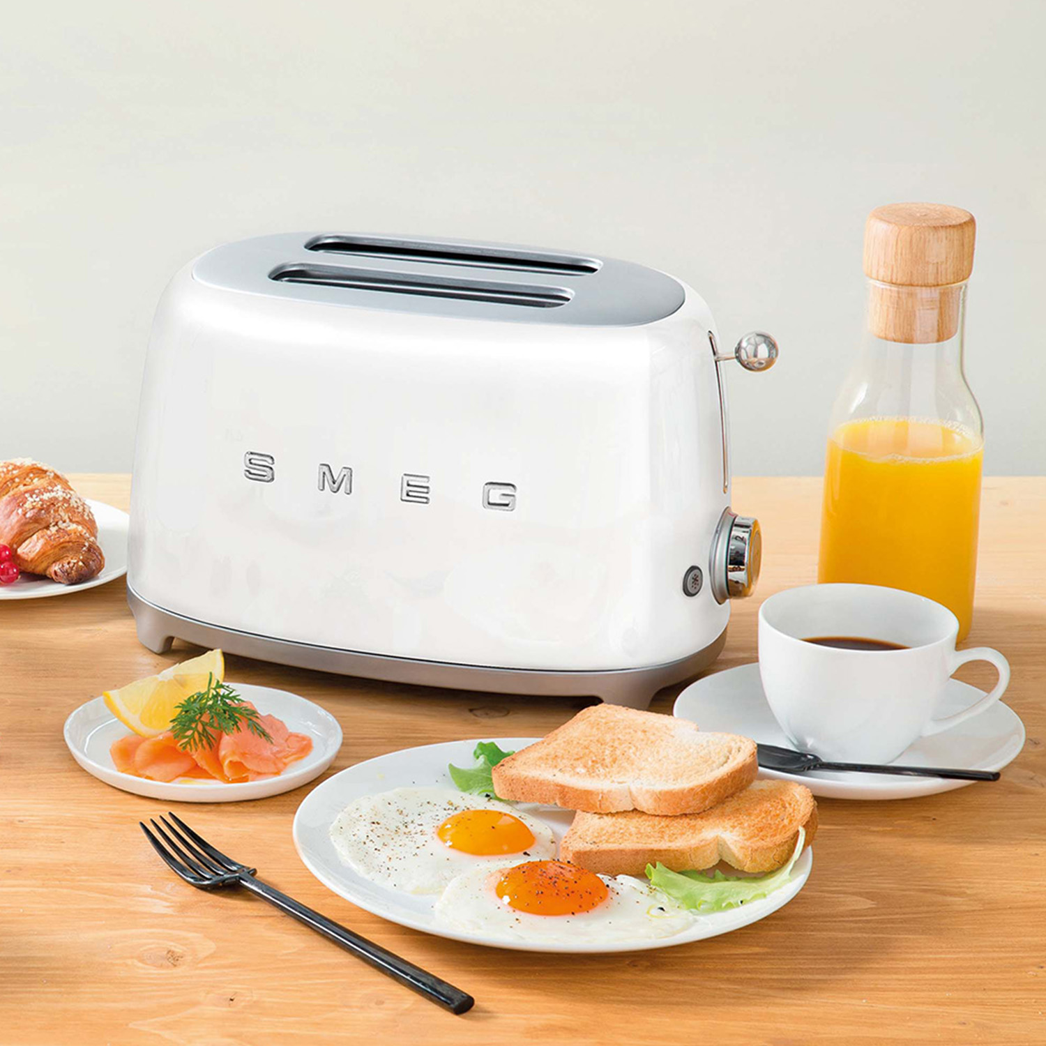 Un tostapane Smeg bianco con elementi per la colazione su un tavolo di legno.