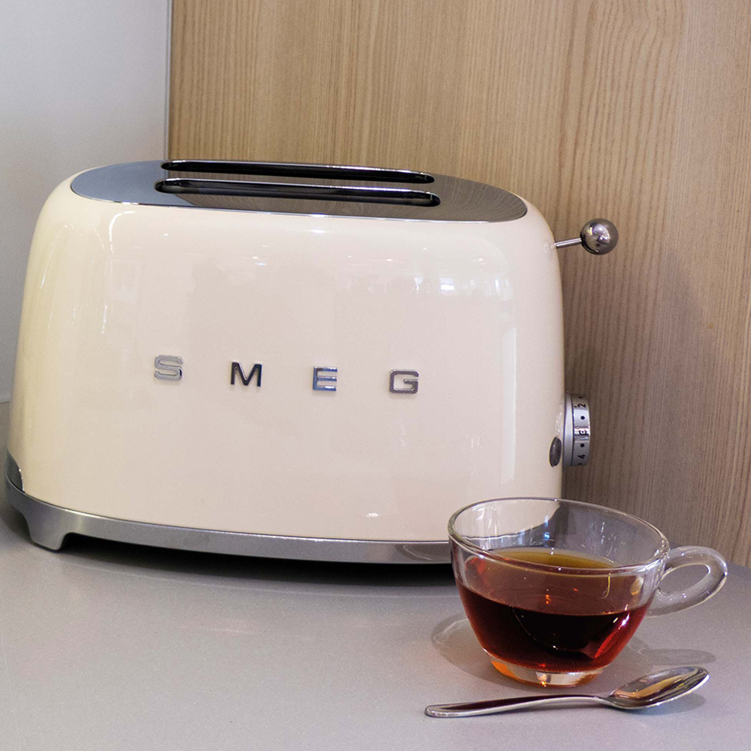 Tostapane SMEG beige con tazza di tè e cucchiaio. Parete in legno dietro.