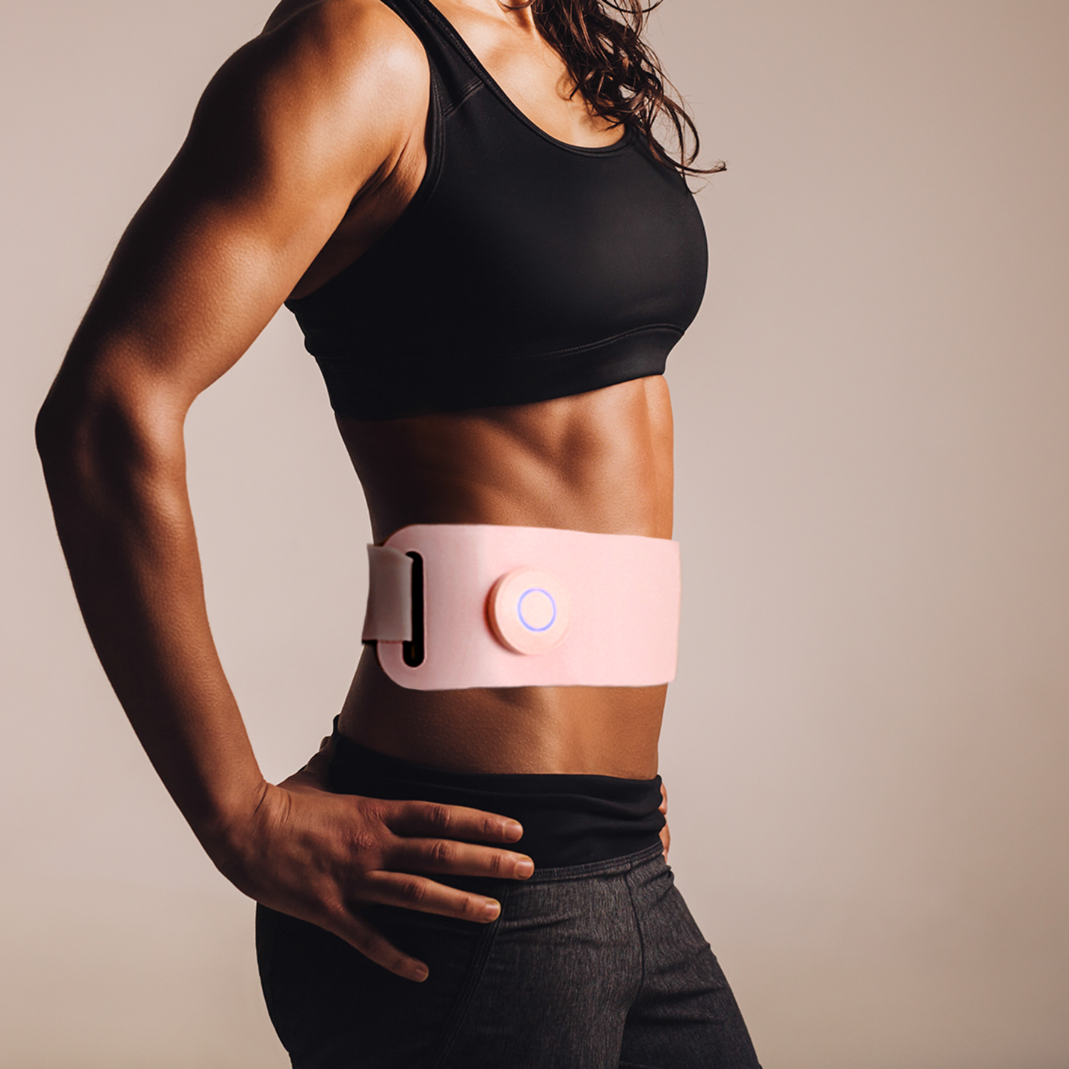 Woman wearing a black sports bra and a pink belt-like device around her waist.