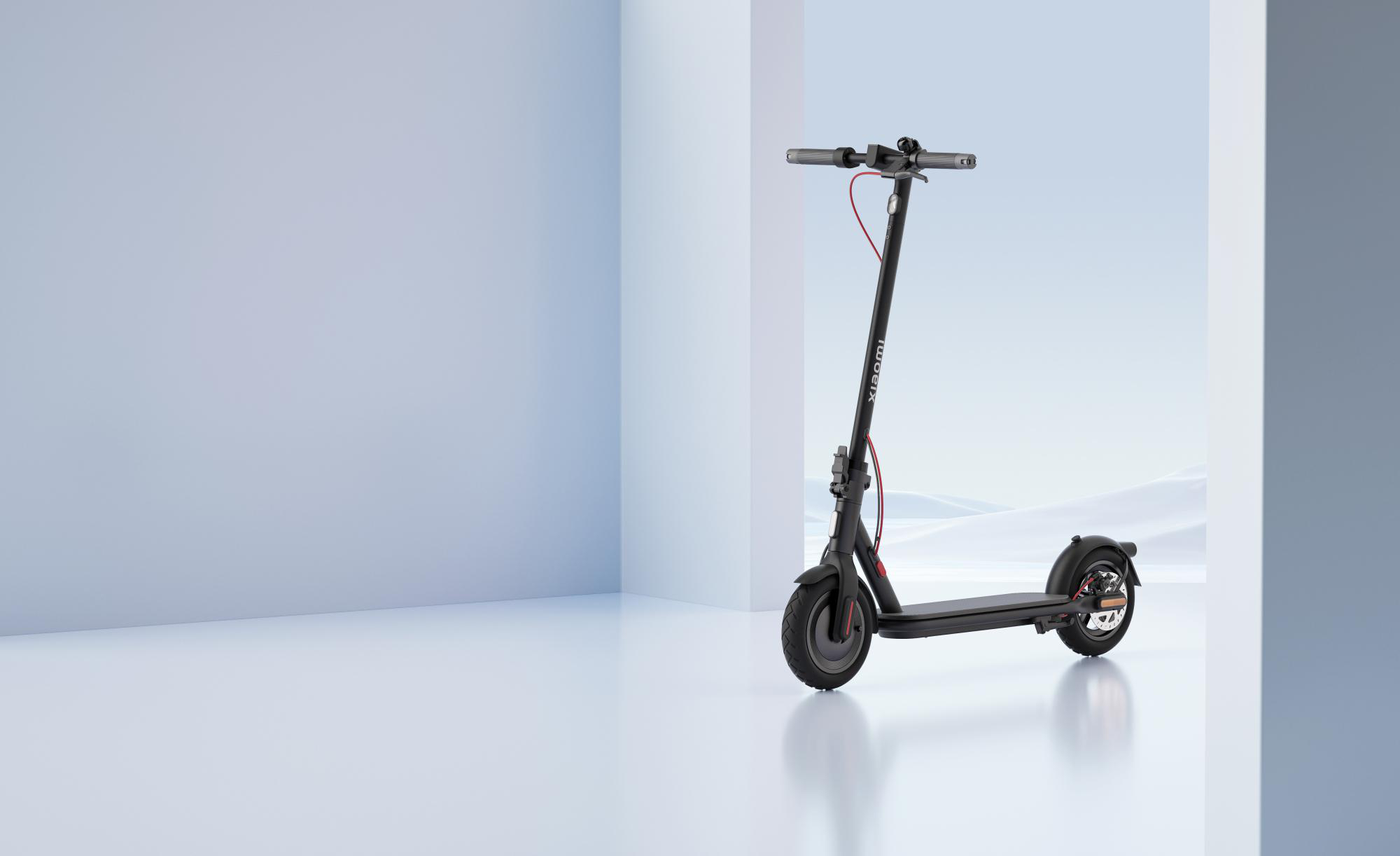 Ein schwarzer Roller steht in einem weißen Raum mit blauer Wand. Der Roller hat ein rotes Kabel.