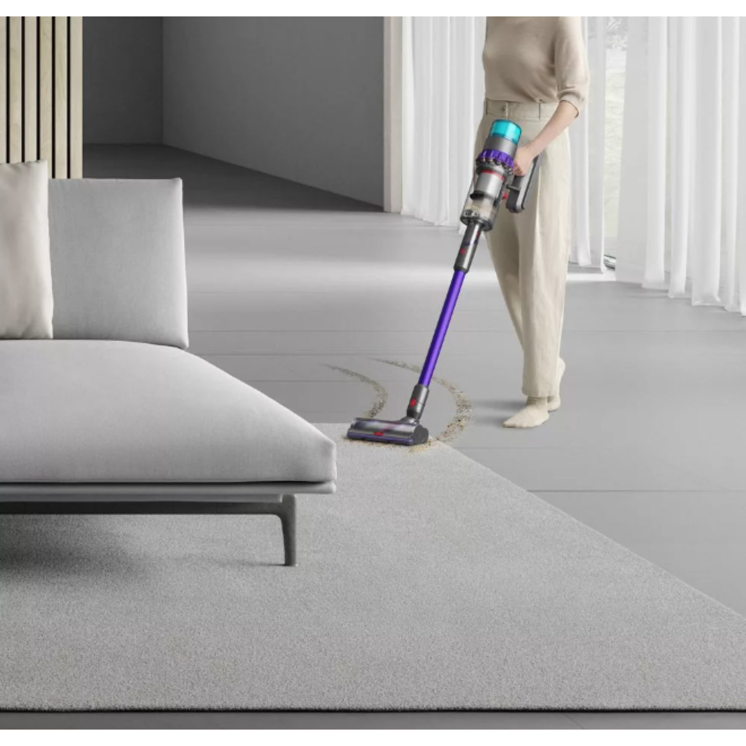 A woman vacuuming a gray carpet with a purple and gray Dyson vacuum cleaner.