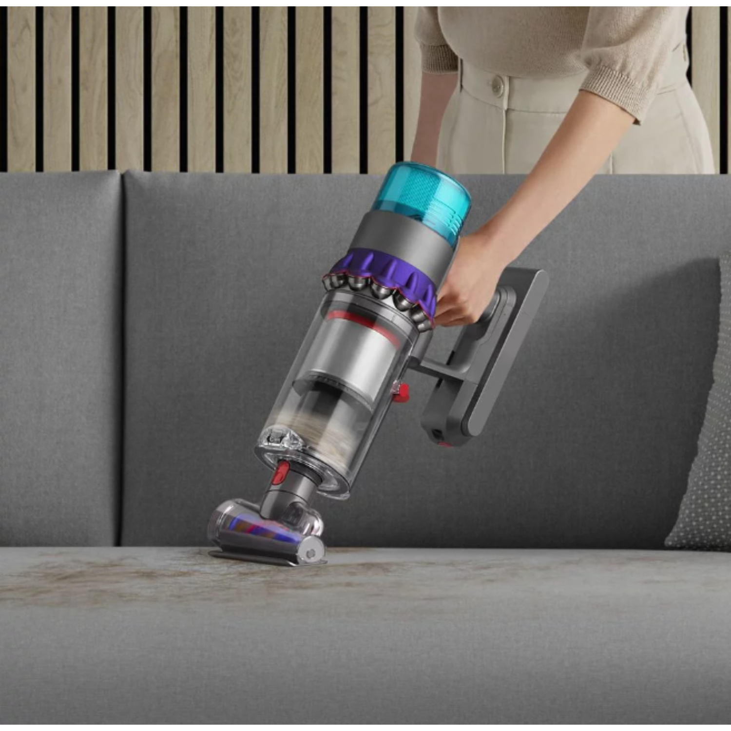 A person vacuuming a couch with a handheld vacuum cleaner.